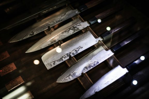 Collection of various kitchen knives displayed on a wooden surface with soft lighting.